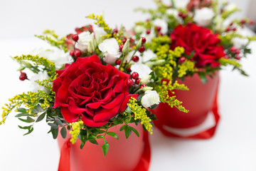 Life-affirming composition of fresh flowers (Rose, Eustoma, Solidaga, Pistachio leaves) and decorative berries in a scarlet cardboard round hat box on a light background