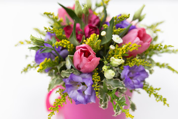 Cute bouquet (pink, yellow, green, purple) of roses, eustoma, gerberas and greenery in a round pink cardboard box with a ribbon on a light background