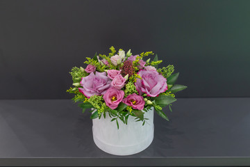 An impressive composition of roses and exotic flowers with leaves in a hat box on a gray background