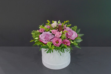 An impressive composition of roses and exotic flowers with leaves in a hat box on a gray background