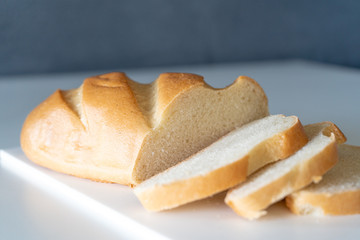 Fresh ruddy long loaf chopped on a white board on a white table. Side view
