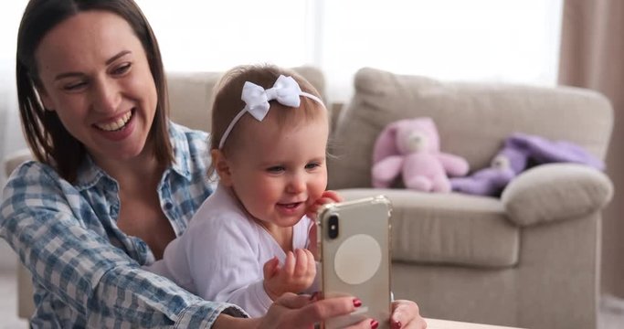 Playful baby girl with mother taking selfie using mobile phone camera at home