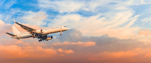 Fototapeta na wymiar Passenger airplane is landing approach gear released, against sunset sky clouds, panorama. Travel aviation, flight, trip.