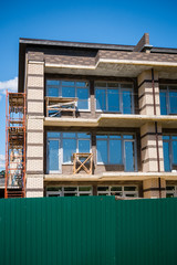 Construction site of unfinished modern brick building with scaffolding and trestle tables behind green fence