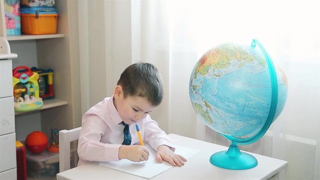 Boy studying planet earth and writes notes in a notebook