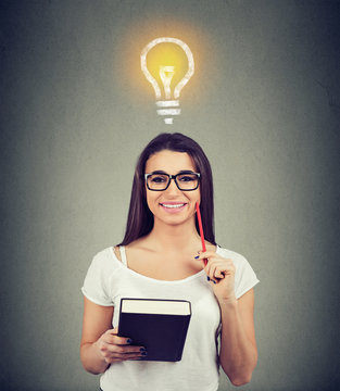 Portrait of a beautiful woman with bright light bulb above head holding a book