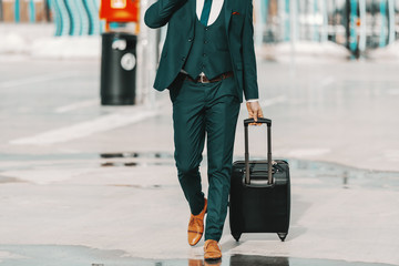 Businessman in formal wear pulling luggage and walking on the street. Business trip concept.