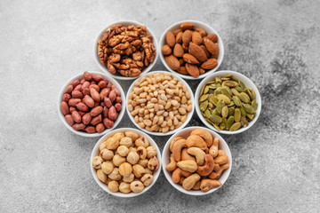Assortment of nuts in white saucers on a concrete background. Food mix background, top view, copy...