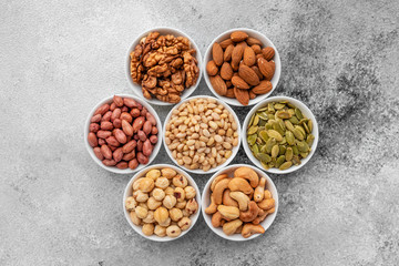Assortment of nuts in white saucers on a concrete background. Food mix background, top view, copy space, banner
