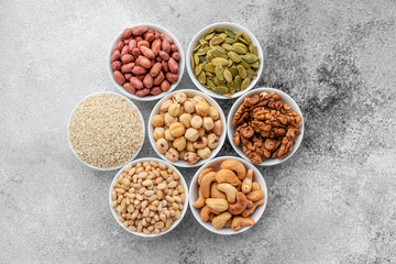 Assortment of nuts in white saucers on a concrete background. Food mix background, top view, copy space, banner