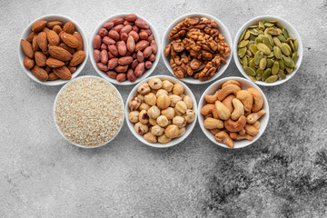 Assortment of nuts in white saucers on a concrete background. Food mix background, top view, copy...