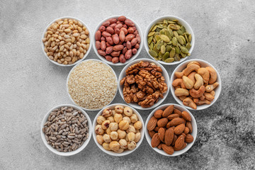 Assortment of nuts in white saucers on a concrete background. Food mix background, top view, copy space, banner