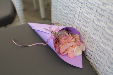 purple bag with pink rose petals to be sprinkled on newlyweds lay on the chair for wedding ceremony guests. Event decoration with fresh flowers