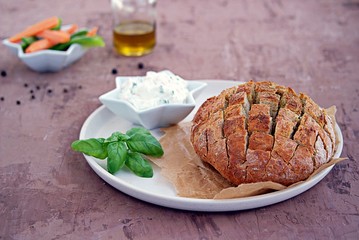 Round baked party bread on a ceramic plate. Served with cream cheese dip and fresh chopped carrots and sweet green pepper. Selective focus