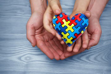 World Autism Awareness day, puzzle or jigsaw pattern on heart with autistic child's and father hands