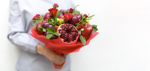 Beautiful bouquet consisting of pomegranate, apples, grapes, plums and scarlet roses in the hands of a woman on a white background as a blank for a greeting card