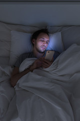 Addiction, nomophobia, insomnia, sleep disorder concept. Male addicted to the smartphone connected 24/7 to internet, lying on bed and using smart phone at late night. 