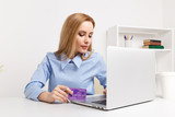 Office woman holding purple credit card and making shopping online at her workplace