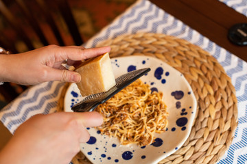 woman hands grating parmesan cheese to homemade spaghetti bolognese, traditional pasta dish with meat and vegetables