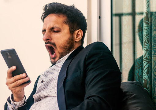 bored man holding smart phone and yawns, front view- image