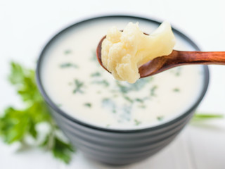 Wooden spoon with cauliflower inflorescence over a bowl of cream soup.