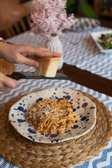 woman hands grating parmesan cheese to homemade spaghetti bolognese, traditional pasta dish with meat and vegetables
