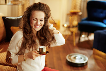 woman with coffee cup and robot vacuum cleaning floor in backgro