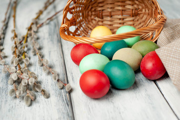 Easter eggs in a basket and willow branches on a wooden background