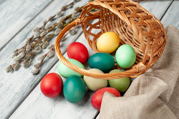 Easter eggs in a basket and willow branches on a wooden background