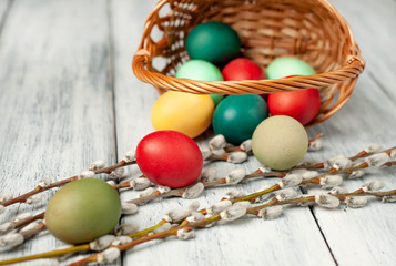 Easter eggs in a basket and willow branches on a wooden background