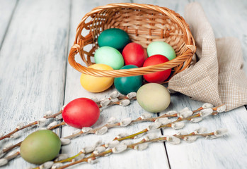 Easter eggs in a basket and willow branches on a wooden background