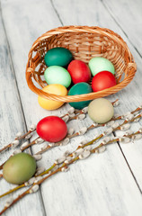 Easter eggs in a basket and willow branches on a wooden background