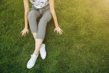 Fashionable hipster girl is sitting on the green grass lawn. Stylish details of hands and legs outdoors. Business woman resting. Student's life free time. Office worker break.