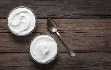 Two glass bowls with white yogurt on old wooden desk.