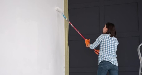 Young woman painting wall with a roller in new home