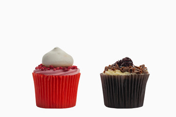 Cupcake in red paper case with pink frosting and raspberry on top and chocolate black forest fairy cake on white, selective focus
