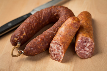 Luftgetrockneter Mettwurst Ring und frische Bierbeißer, zwei Salami Sorten aus Schweinefleisch mit Messer auf Holz Brett 