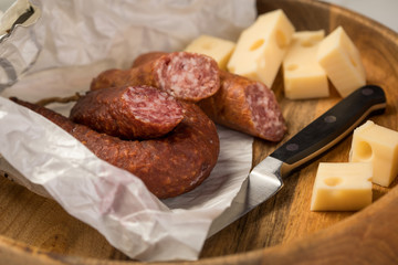 Ringwurst Salami, Bierbeißer Wurst und Edamer Käse in Wachspapier mit Messer auf Vesper Holzbrett