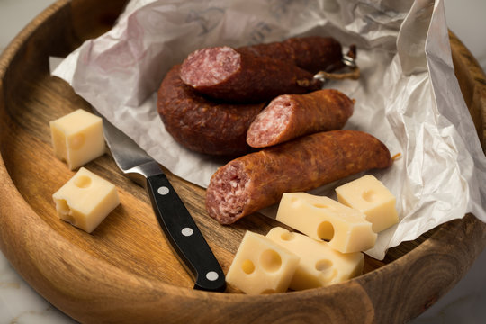 Ringwurst Salami, Bierbeißer Wurst und Edamer Käse in Wachspapier mit Messer auf Vesper Holzbrett