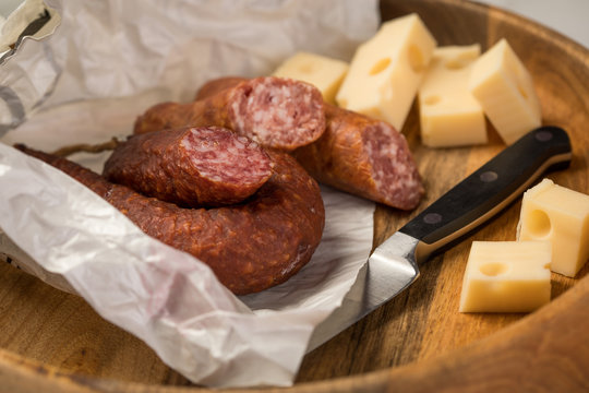 Ringwurst Salami, Bierbei&szlig;er Wurst und Edamer K&auml;se in Wachspapier mit Messer auf Vesper Holzbrett