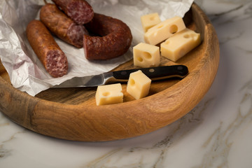 Fototapeta na wymiar Ringwurst Salami, Bierbeißer Wurst und Edamer Käse in Wachspapier mit Messer auf Vesper Holzbrett