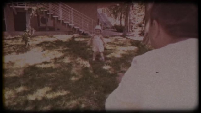 Family video archive. Retro camera 8 mm. Old film. A young father holds a small daughter in his arms and kisses her against the background of green trees