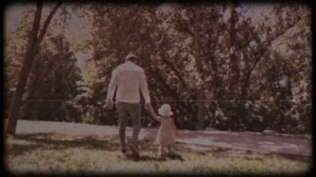 Family video archive. Retro camera 8&nbsp;mm. Old film. A young father holds a small daughter in his arms and kisses her against the background of green trees