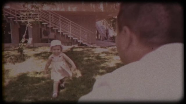 Family video archive. Retro camera 8 mm. Old film. A young father holds a small daughter in his arms and kisses her against the background of green trees