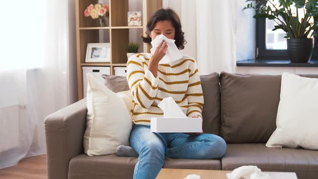 healthcare, cold, hygiene and people concept - sick woman taking paper tissue from box and blowing her nose at home