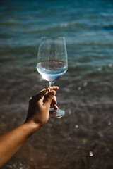 blue sea background wine glass with brilliant liquid natural light tanned female hand