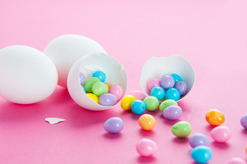 colourful easter eggs spilling out of a white egg shell on a pink background