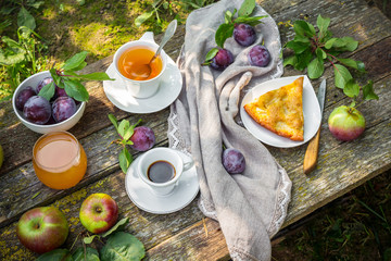 Lunch breakfast on the terrace in the garden. Orange juice, pie, coffee, tea, apples on a wooden...