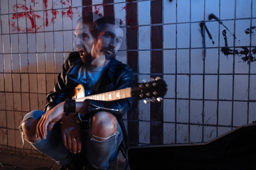 A street musician playing on guitar in the underpass. Two facial expressions Express boredom and anger.