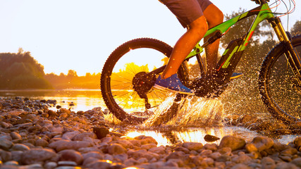 SUN FLARE: Unrecognizable sportsman riding a mountain bike in a shallow stream.